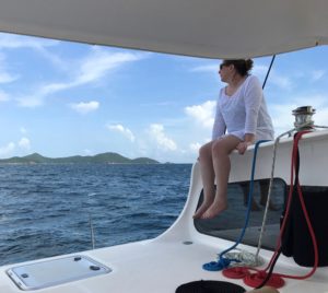 Woman sits on top of cabin of a boat wistfully looking out over water on sunny day.