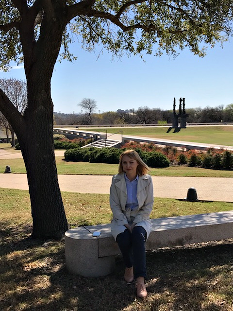 Magdalena Bus Woman seated on a stone bench under the shade of a tree in front of a museum on a sunny winter day.