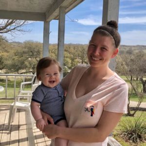 Woman poses on porch of a ranch house with smiling child.