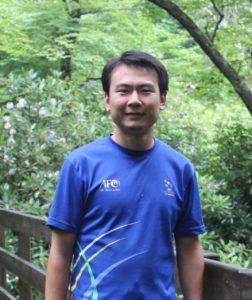 Muyi Liu Man poses for photo on a wooden walkway in forested area