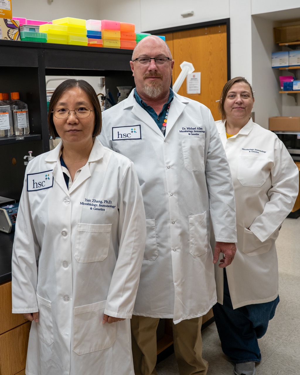 Three members of the Michael Allen Lab in white lab coats in a lab at UNT Health Fort Worth