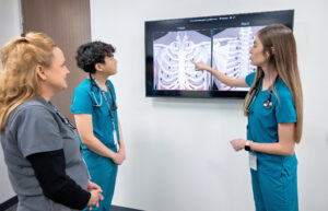 A student points to an X-ray while another student and an instructor watch.