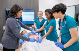 An instructor uses a medical mannequin to teach three students.