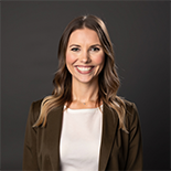 K McKenna headshot with a gray background wearing a brown blazer