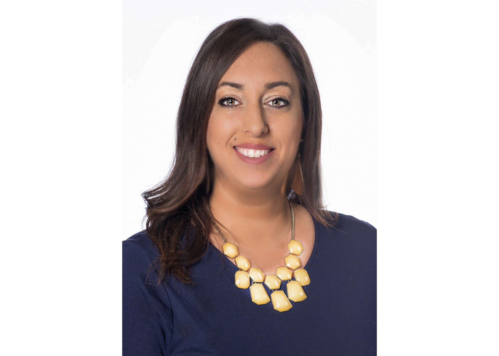 person with long brown hair smiling with navy dress and jewelry on white background