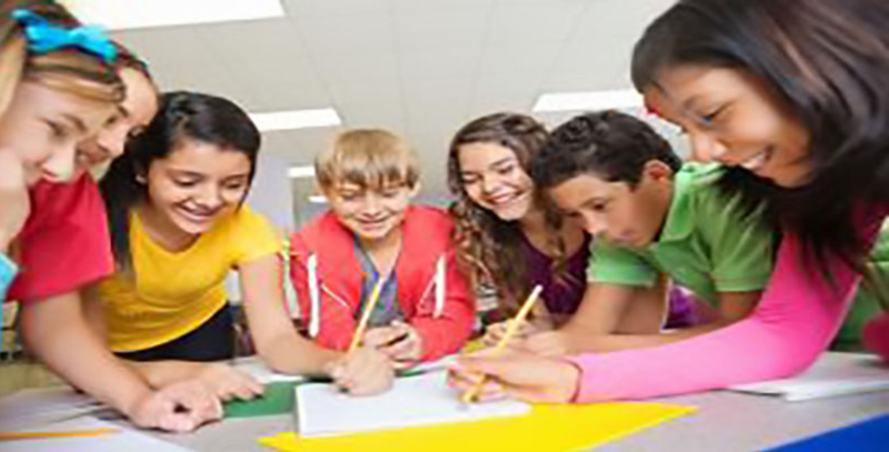 Children leaning over a table marking on a paper with pencils.