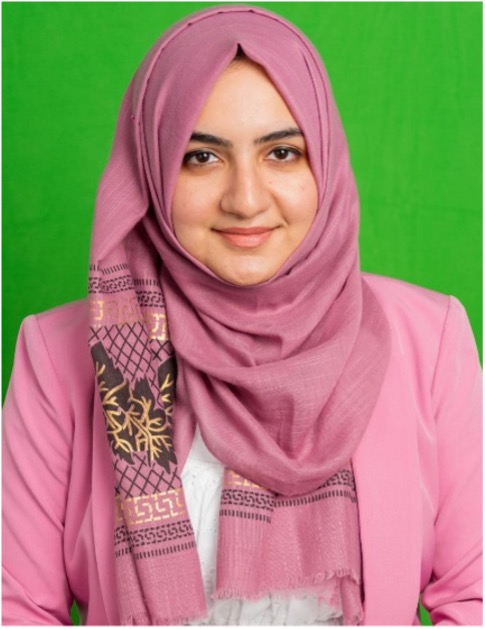 Headshot of Dr. Sahara Ali wearing a pink hijab and matching blazer, smiling at the camera against a green background.
