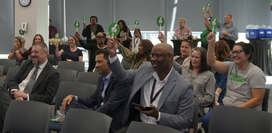 A group of professionals at OIIA’s Playlist Battle event, many of whom are excitedly displaying green thumbs-up signs to vote for their favorite performance.