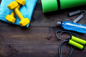Fitness Equipment. Jump Rope, Dumbbells, Expander, Mat, Water On Dark Wooden Background Top View Copy Space