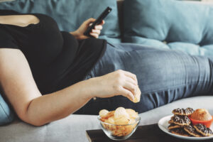 Obese Woman Laying On Sofa Eating Chips